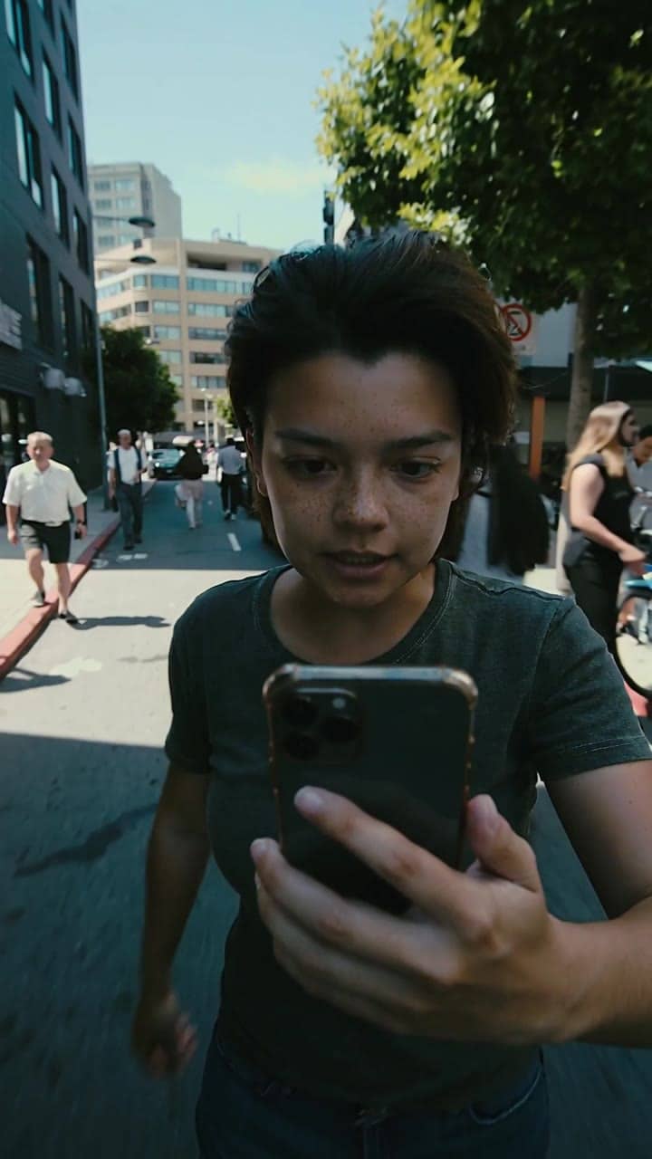 Ejemplo de video IA de Kling 2.5 Turbo: Ultra-realistic walking selfie shot filmed with a smartphone held in one hand. The person is spee...