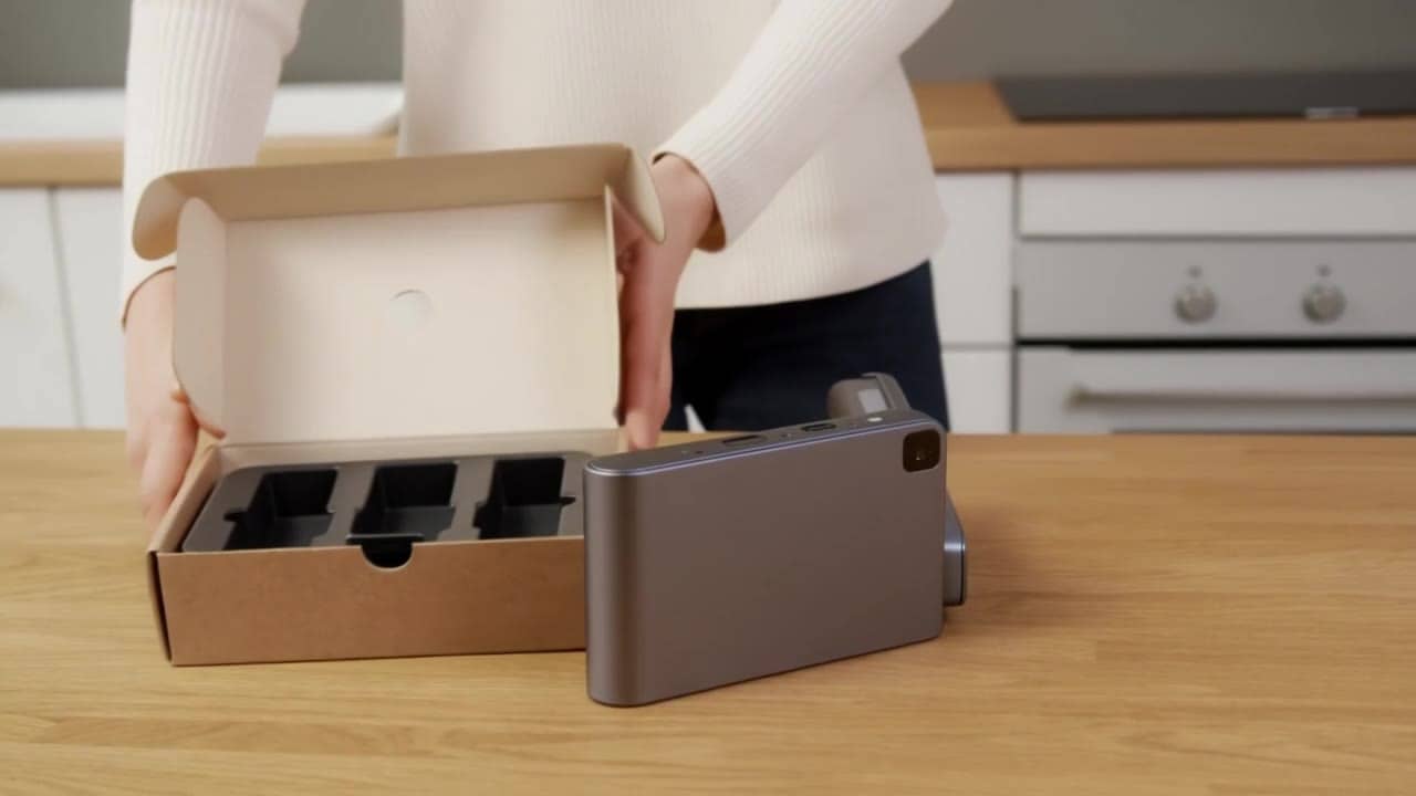 Exemple video IA Luma Ray 2: Wide 16:9 full-body unboxing video in a clean studio/kitchen setting. A person is fully visible (head-to-toe...