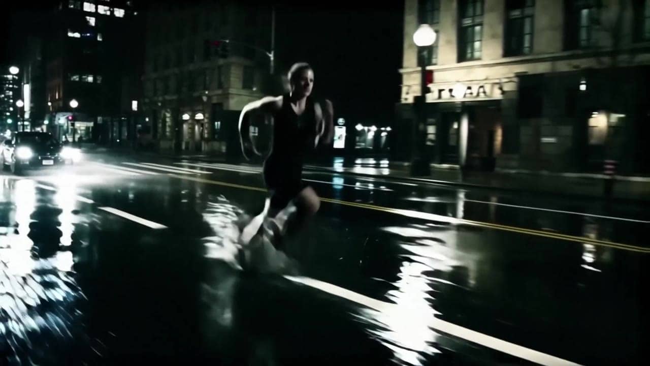 Ejemplo de video IA de LTX Video 2.0 Fast: Wide 16:9 cinematic action shot, a runner sprints through a rainy city street at night, water...