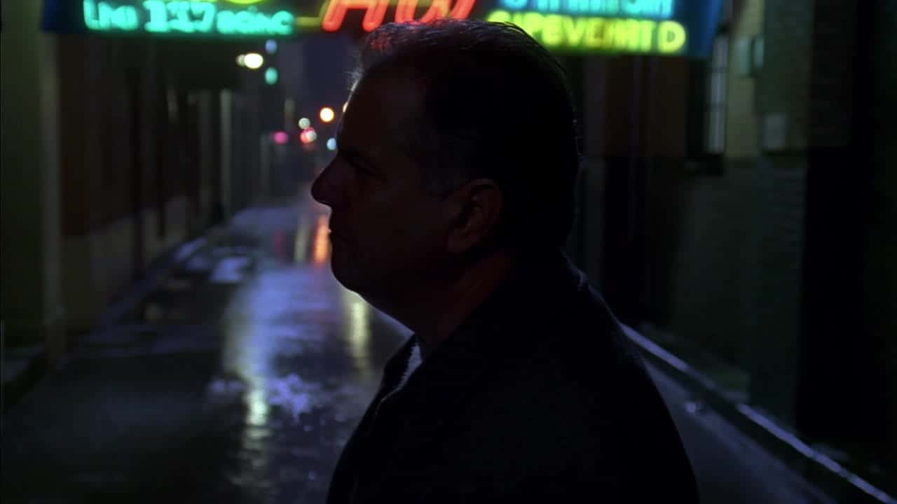 MiniMax Hailuo 02 Standard AI video example: Close-up profile of a middle-aged man standing under a neon sign in a rainy alley at night...