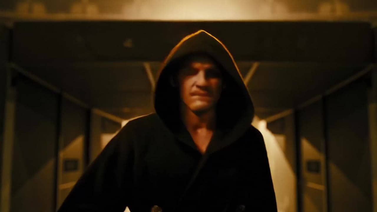 Ejemplo de video IA de LTX 2.3 Fast: A powerful boxer walks alone through a dark arena tunnel toward the ring, athletic frame wrapped in...